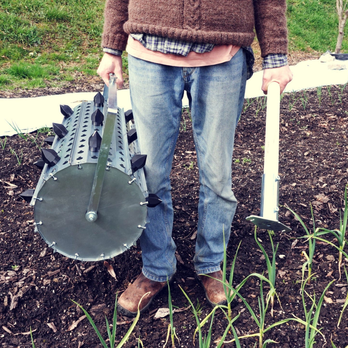 A person carrying Green Tools Tech Rolling Dibbler used for precise no-dig market garden transplanting and cover crop crimping on biointensive beds